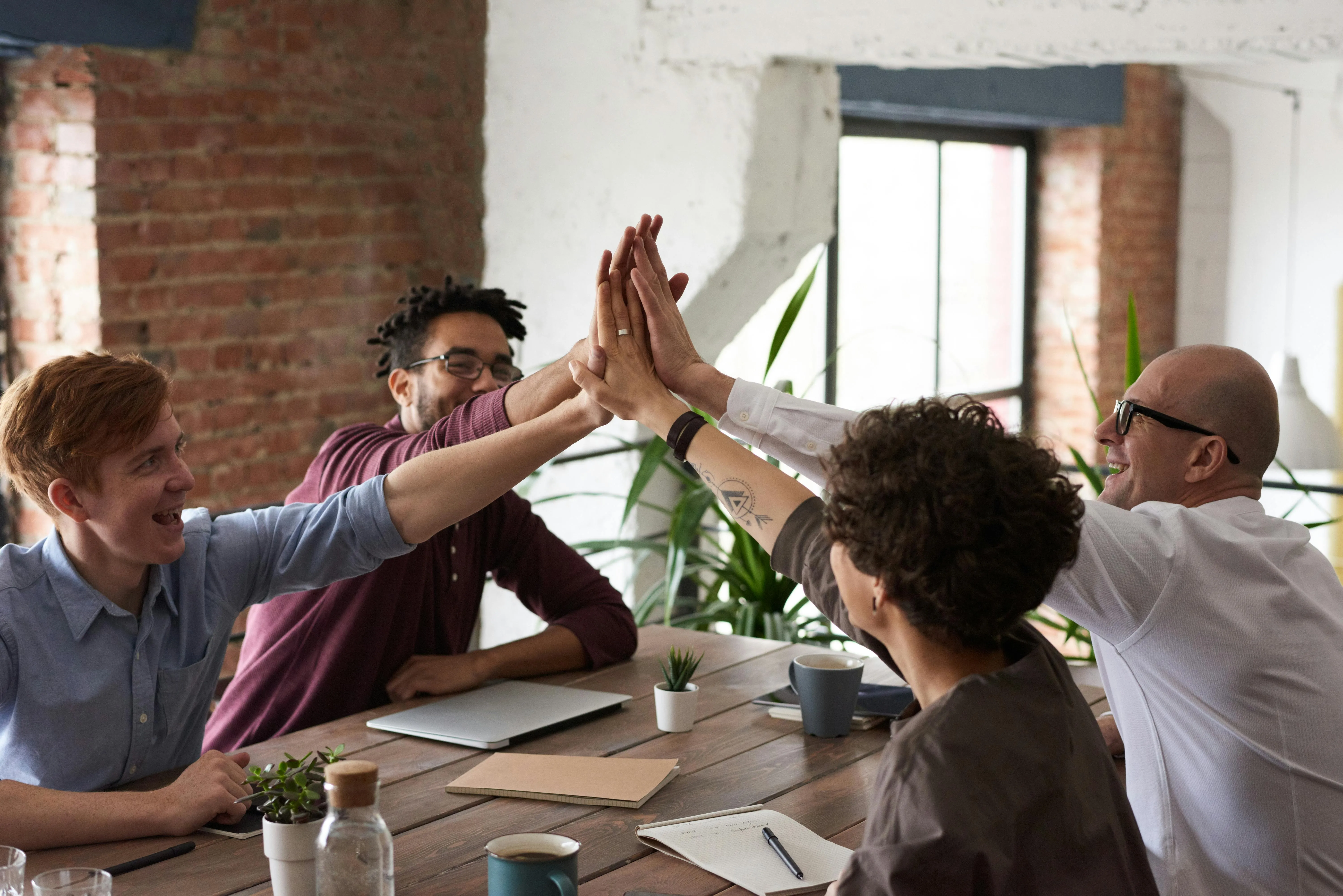 Grupo de colegas comemorando com high five em reunião.