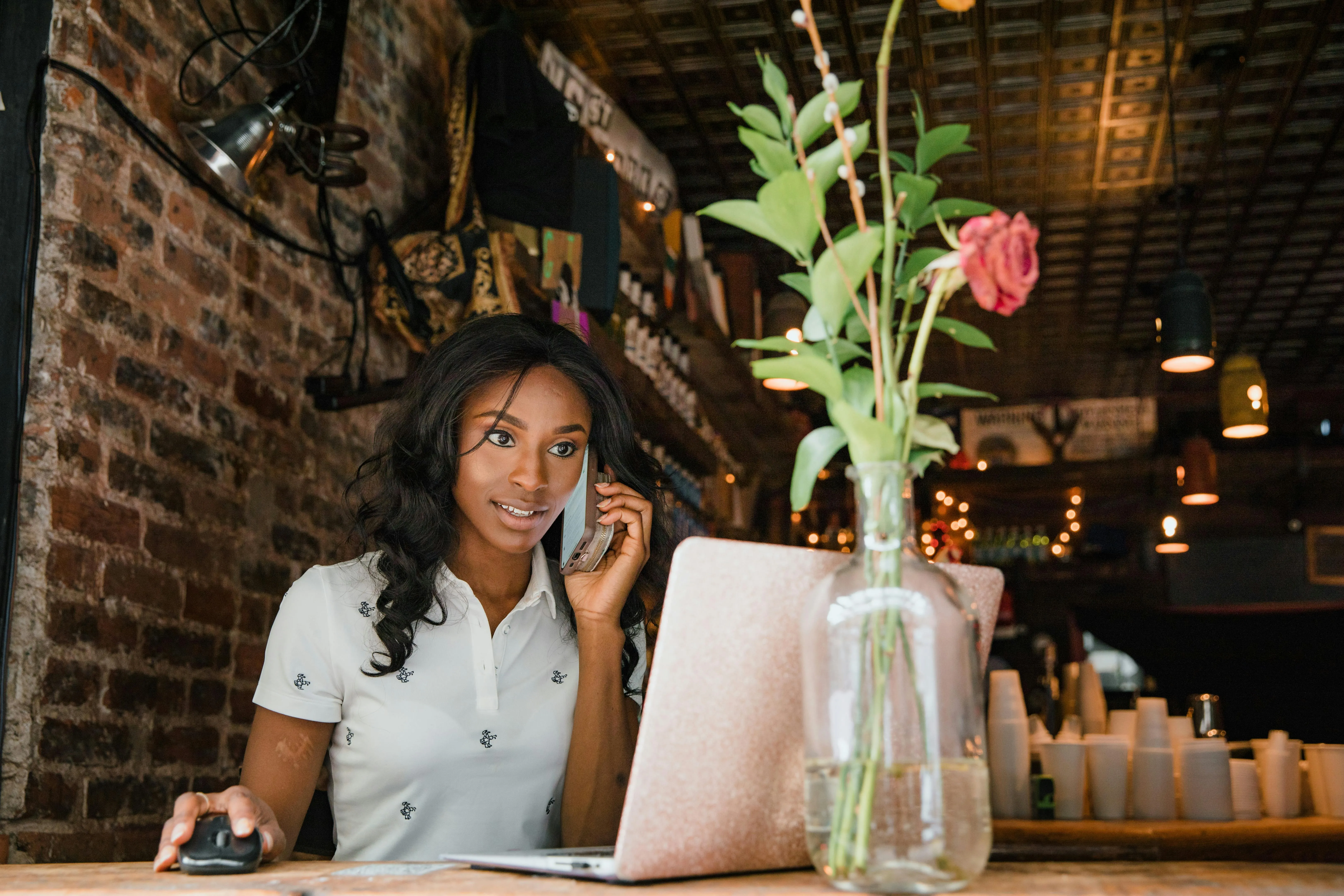 Mulher falando ao telefone e usando laptop em ambiente de café.