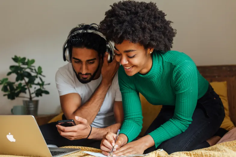 Casal estudando junto com notebook e anotações na cama.
