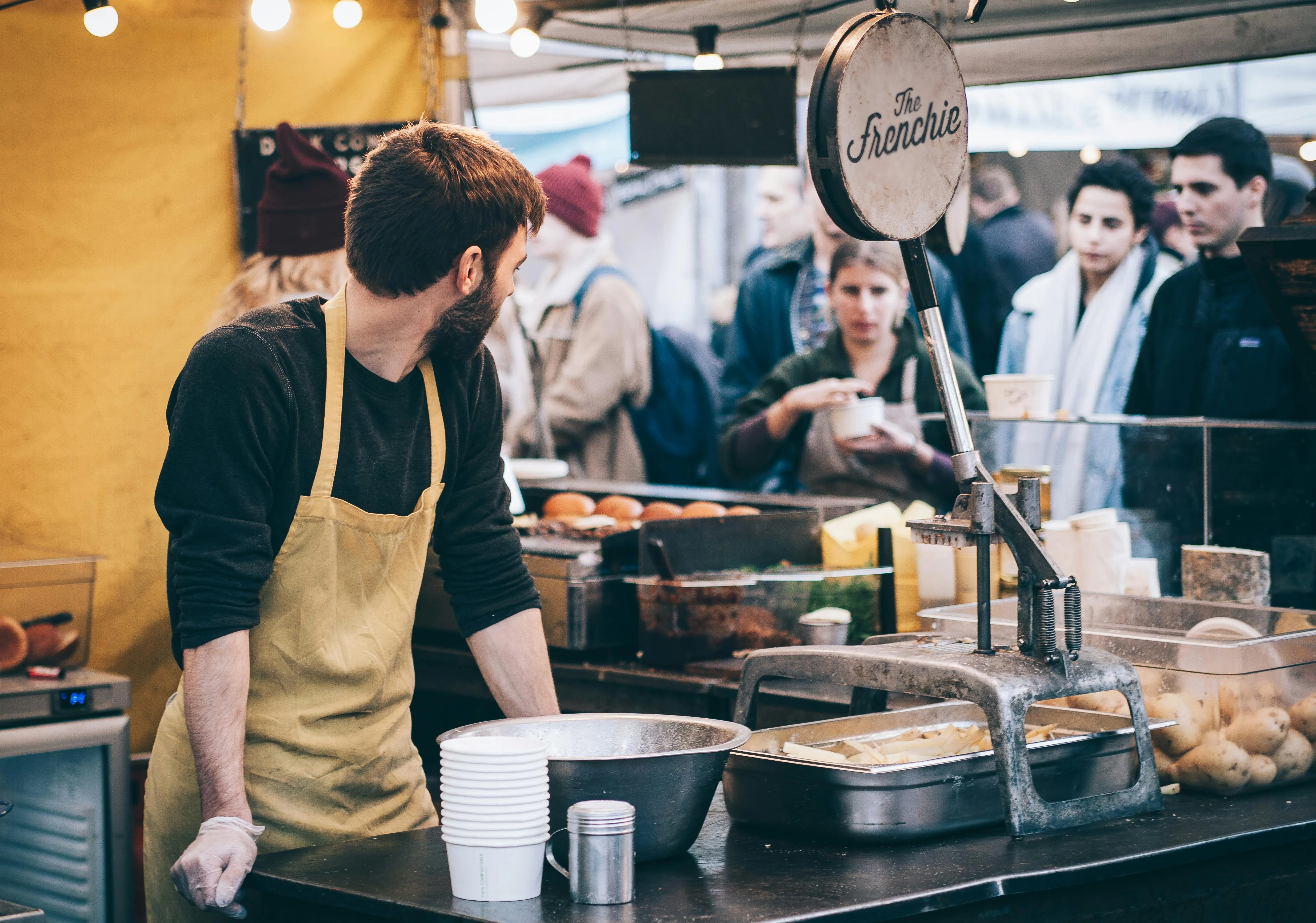 Homem vende comida francesa em feira movimentada com foco na culinária francesa.