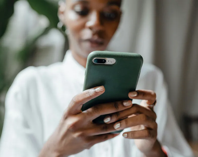 #FotoDescrição: Pessoa segurando um celular com as duas mãos, concentrada na tela, em ambiente interno com luz suave.